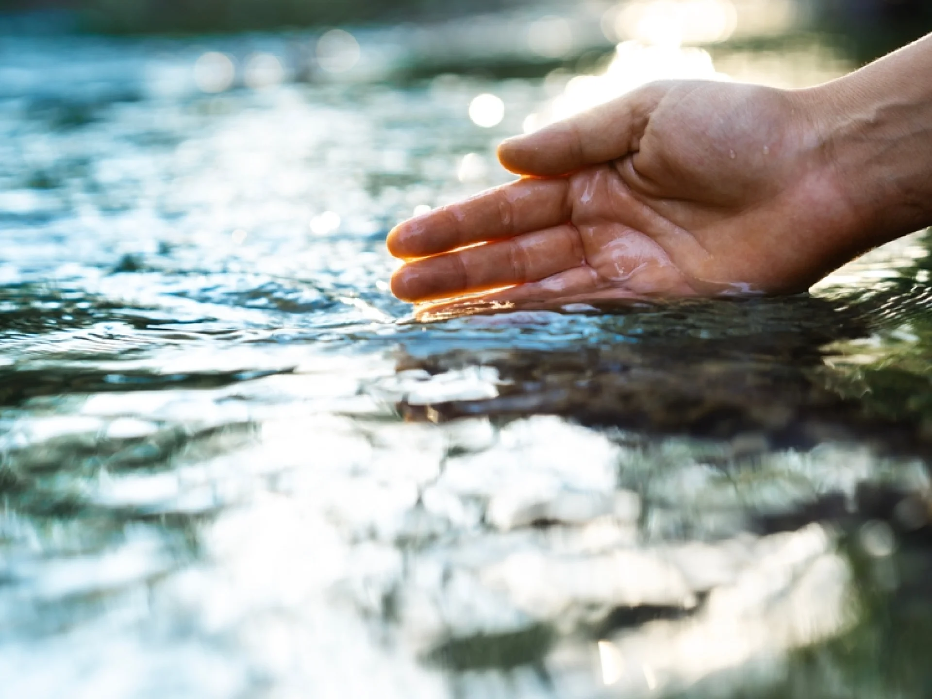 Hand taucht in das Wasser eines Flusses ein