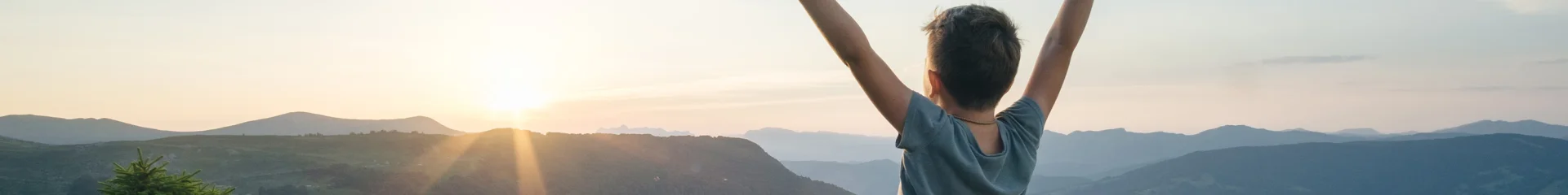 Petit garçon, les bras levés face à un paysage de montagne