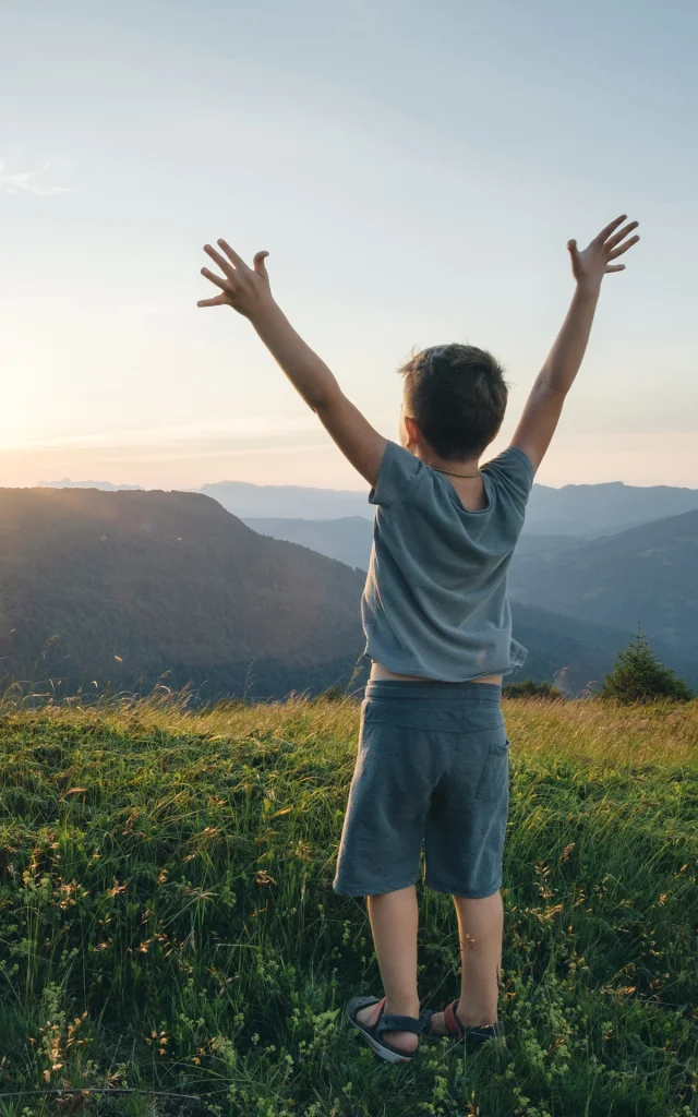 Little boy, arms raised in front of a mountain landscape