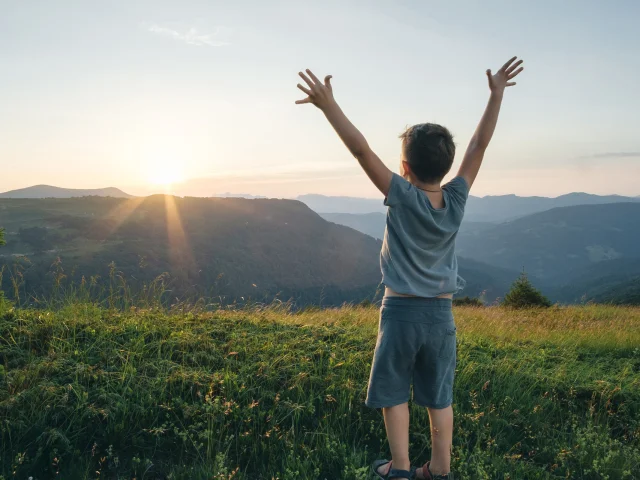 Petit garçon, les bras levés face à un paysage de montagne