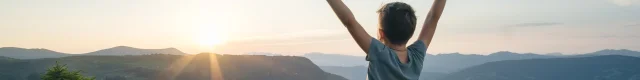 Petit garçon, les bras levés face à un paysage de montagne