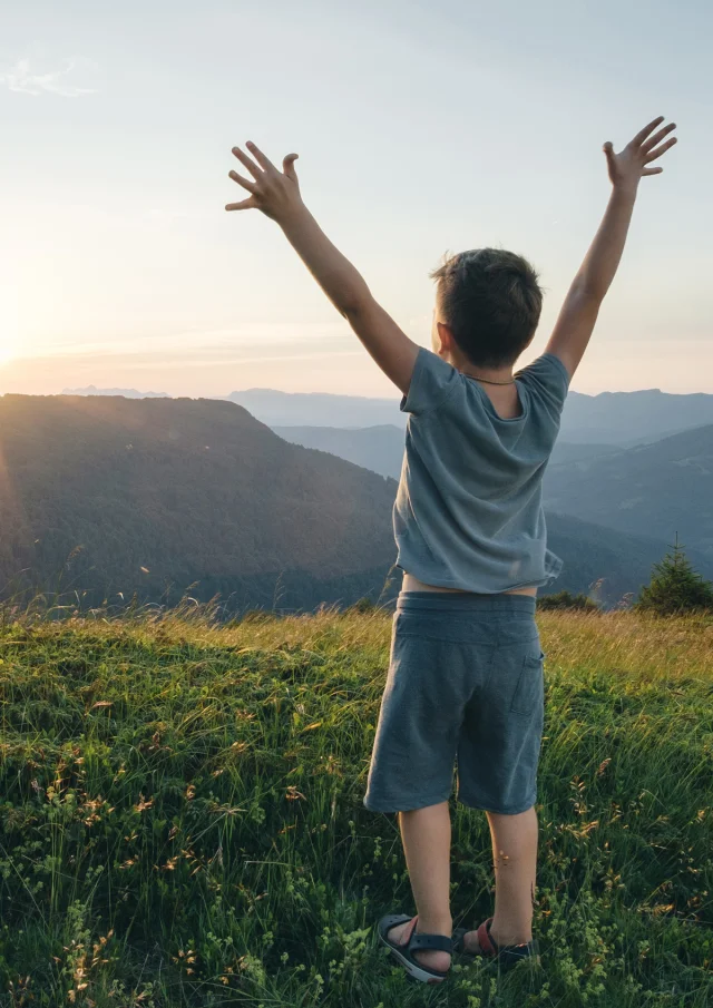 Little boy, arms raised in front of a mountain landscape