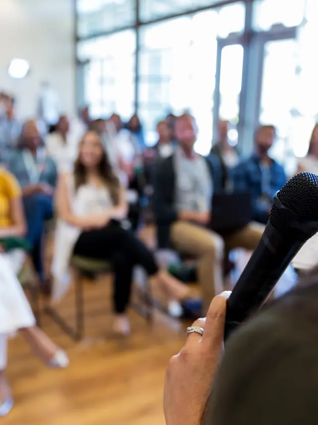 Confident female business conference speaker addresses a large group of business people.