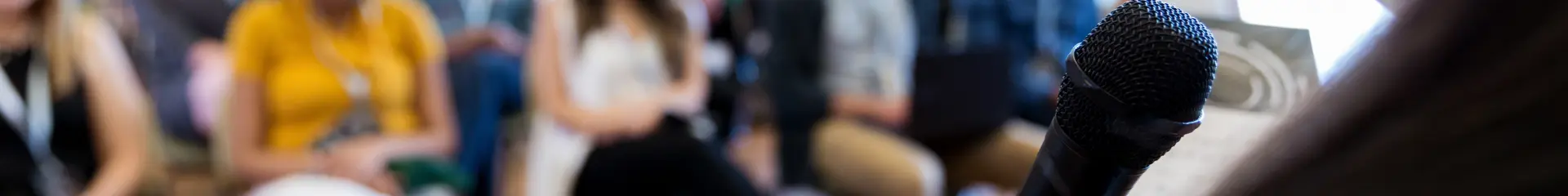 Confident female business conference speaker addresses a large group of business people.