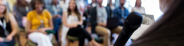 Confident female business conference speaker addresses a large group of business people.
