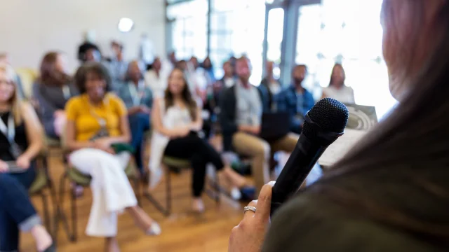 Confident female business conference speaker addresses a large group of business people.