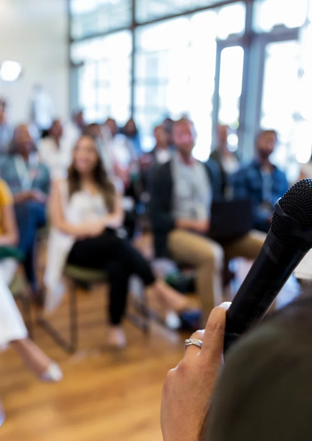 Confident female business conference speaker addresses a large group of business people.
