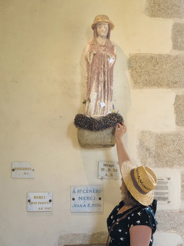 Femme piquant une aiguille aux pieds de la statue de Saint Céneri