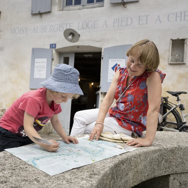 Une grand-mère avec sa petite-fille regardant un plan devant l'office de tourisme de Saint-Céneri-le-Gérei