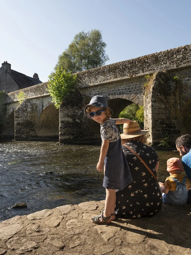 Une famille assise sur les bords de la Sarthe face au pont en pierre de Saint-Céneri-le-Gérei