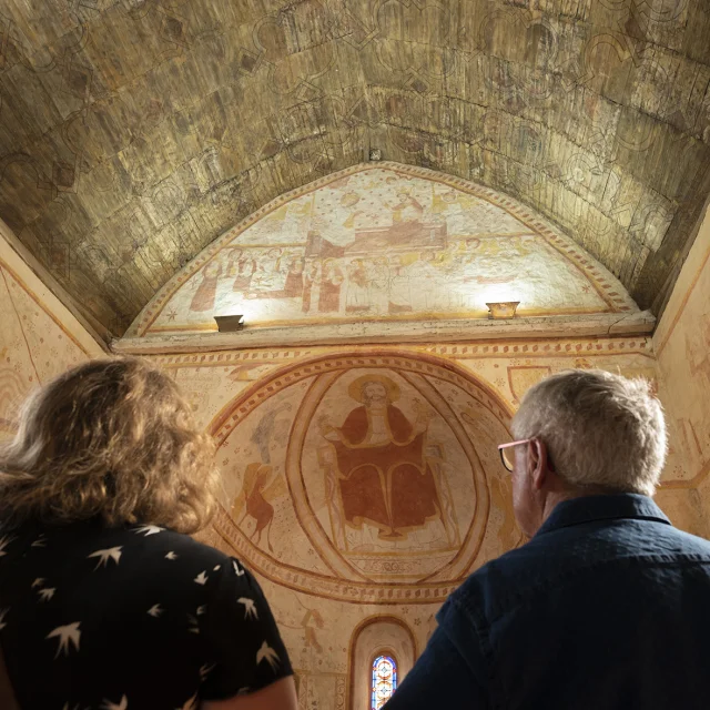 Un homme et une femme admirant les peintures murales de l'intérieur de l'église de Saint-Céneri-le-Gérei