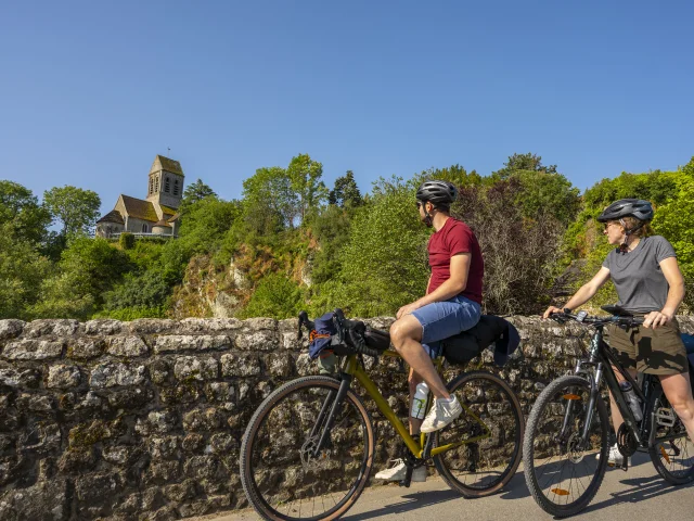 Deux cyclistes regardant l'église romane de Saint-Céneri-le-Gérei, sur La Vélobuissonnière