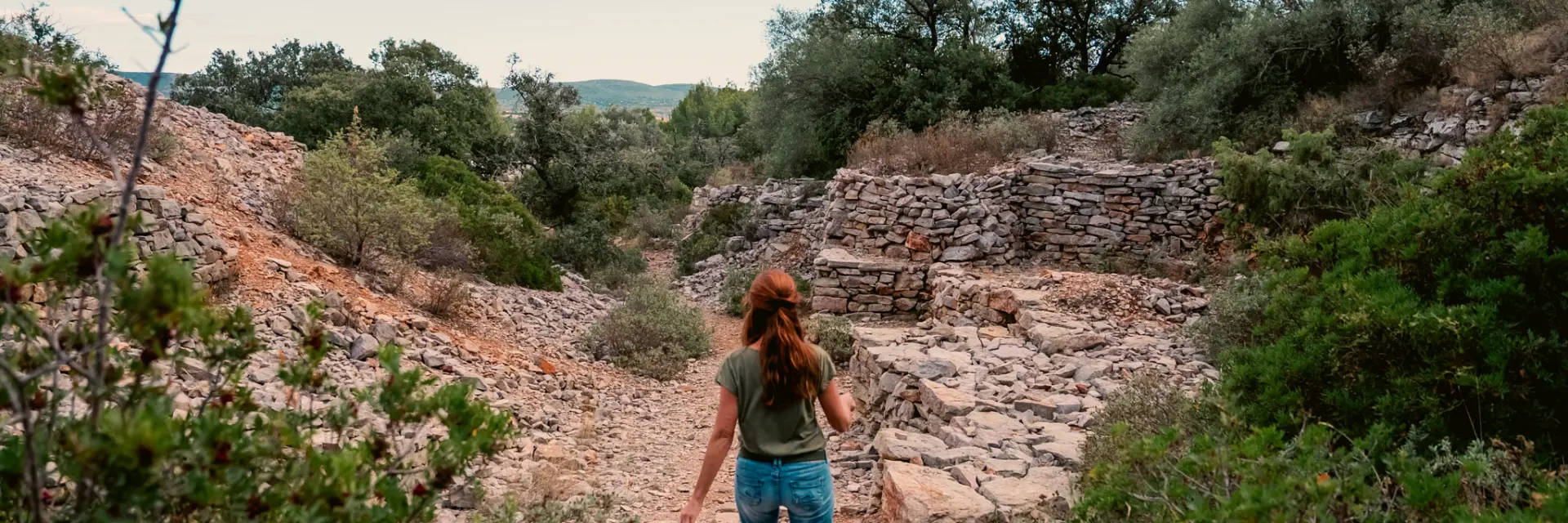 Les capitelles de Poussan,Poussan, capitelles, garrigue, sentier, chemin, pierres sèches, paysage, nature, végétation méditerranéenne, collines, rochers, arbustes, pins, randonnée, balade, promenade, marche, découverte, tourisme nature, outdoor, femme, silhouette, de dos, visiteur, touriste, ciel, ensoleillé, lumière naturelle, été, calme, sauvage, authentique