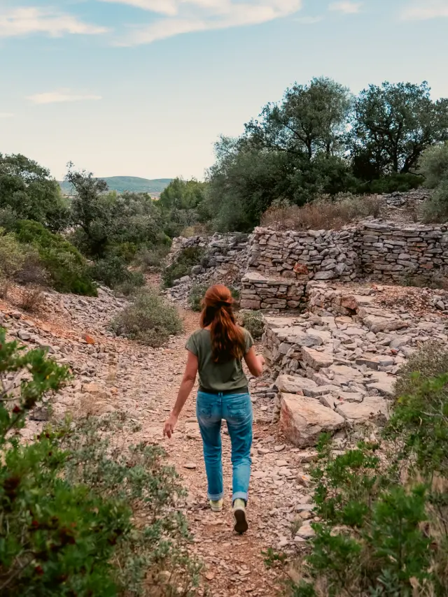 Les capitelles de Poussan,Poussan, capitelles, garrigue, sentier, chemin, pierres sèches, paysage, nature, végétation méditerranéenne, collines, rochers, arbustes, pins, randonnée, balade, promenade, marche, découverte, tourisme nature, outdoor, femme, silhouette, de dos, visiteur, touriste, ciel, ensoleillé, lumière naturelle, été, calme, sauvage, authentique