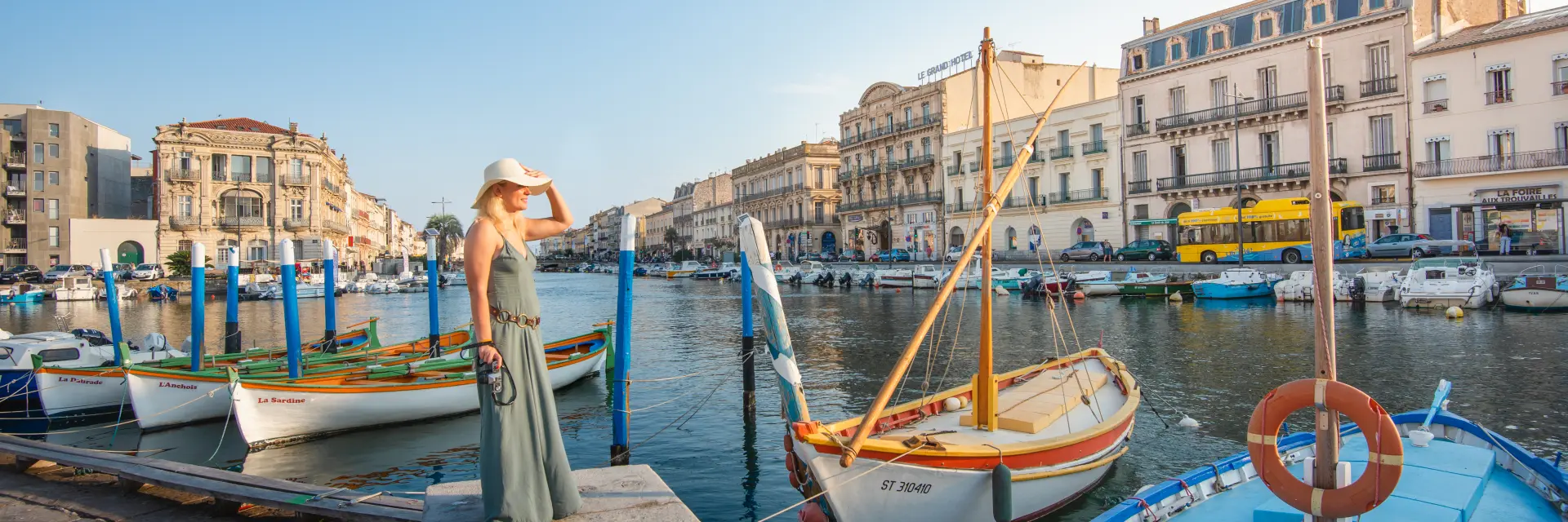 A young woman on the quays of Sète, with a view of the canals and traditional boats.woman, alone, boat, landscape, dress, sky, water