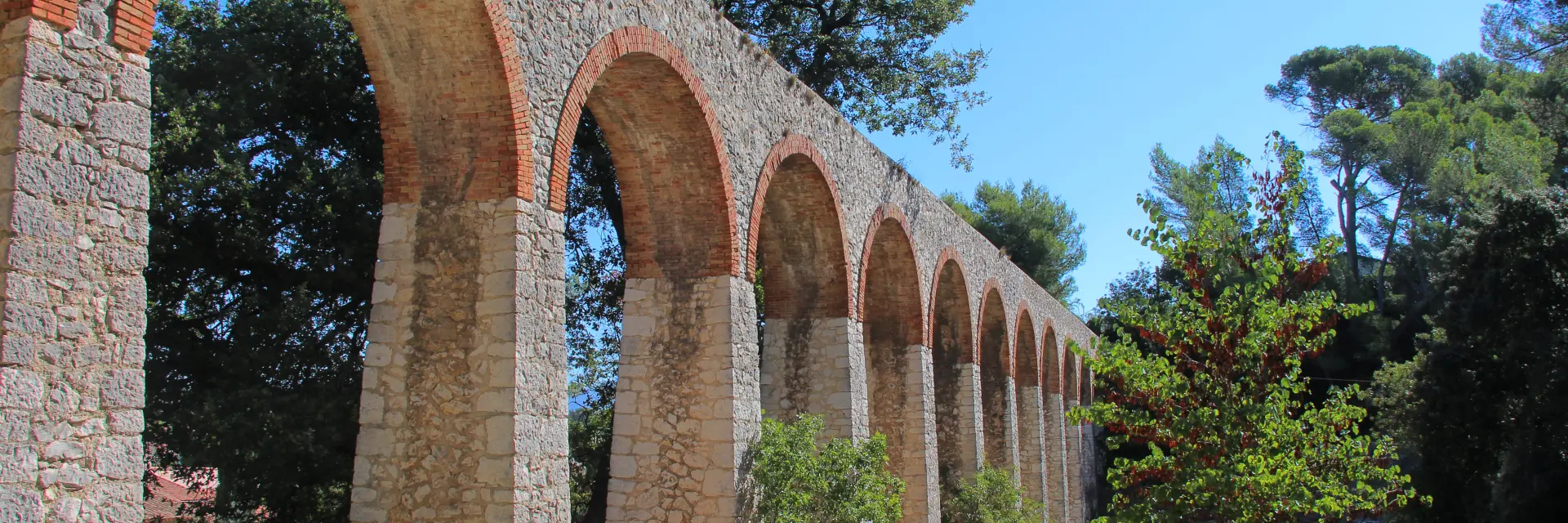 Aqueduc en pierre aux arches élevées entouré de végétation sur un sentier de La Penne-sur-Huveaune.