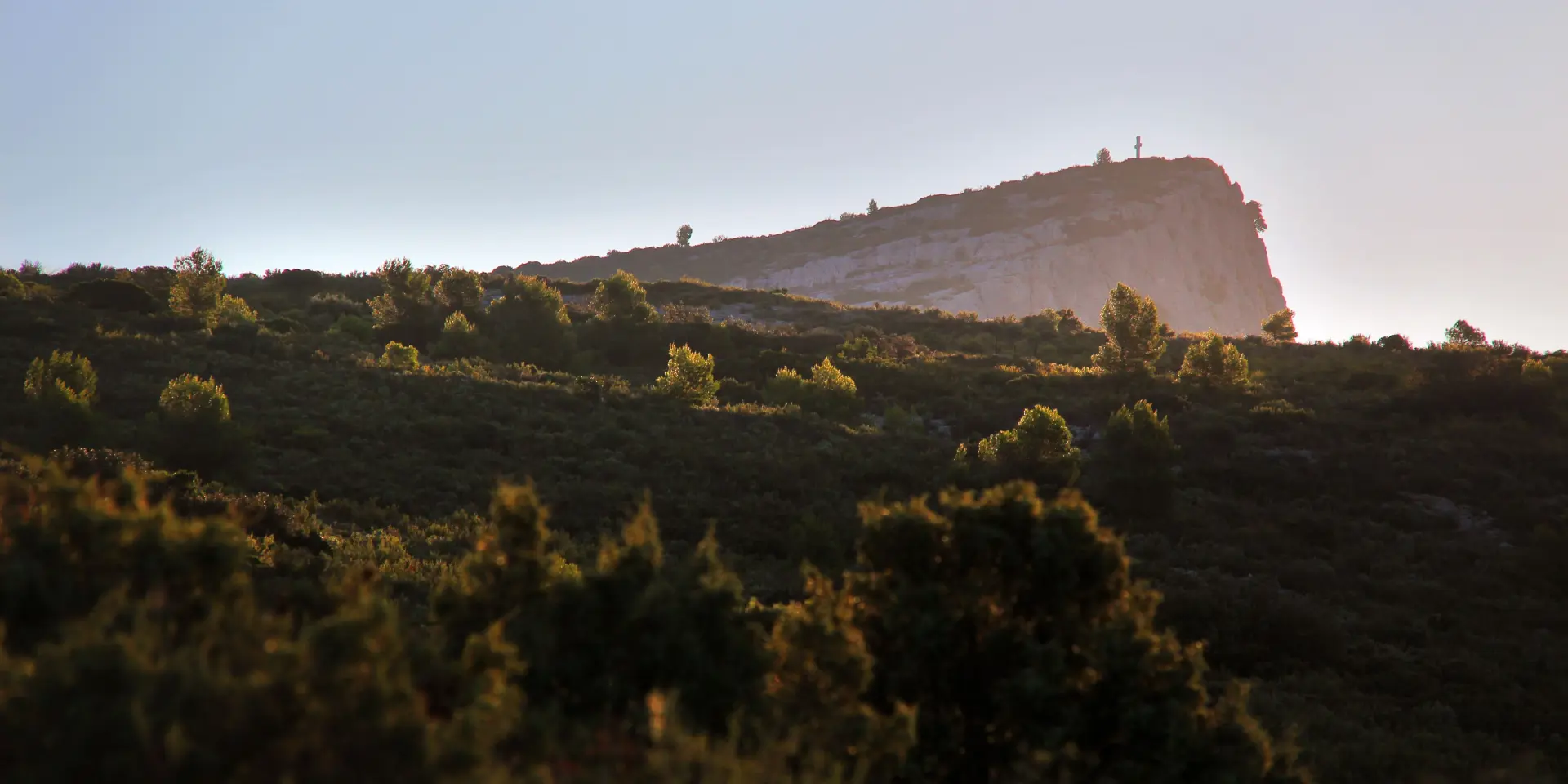 Vue du massif du Garlaban en Provence, colline rocheuse éclairée par la lumière dorée du lever du soleil, entourée de végétation méditerranéenne.
