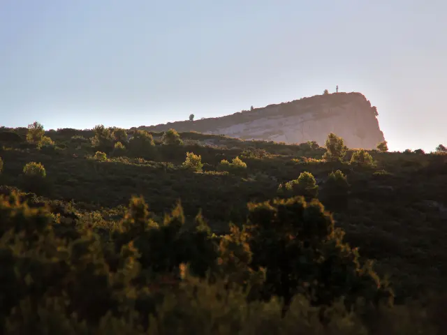 Vue du massif du Garlaban en Provence, colline rocheuse éclairée par la lumière dorée du lever du soleil, entourée de végétation méditerranéenne.