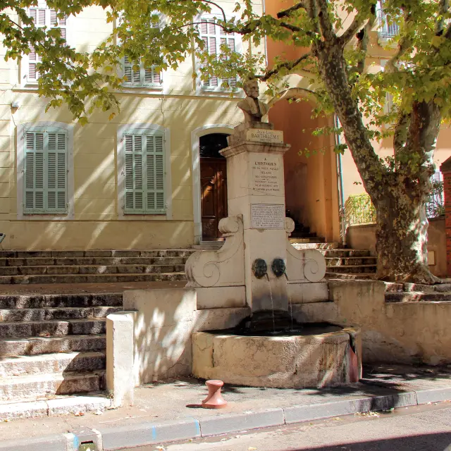 La Fontaine Barthélémy dans le centre historique d’Aubagne, entourée d’escaliers, d’arbres et d’une façade provençale éclairée par le soleil.