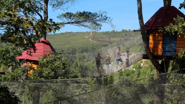 Enfants jouant sur un parcours en filets suspendus entre les arbres dans un parc de loisirs en pleine nature.