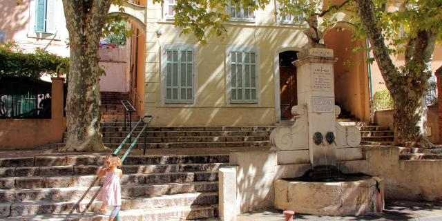 La Fontaine Barthélémy dans le centre historique d’Aubagne, entourée d’escaliers, d’arbres et d’une façade provençale éclairée par le soleil.