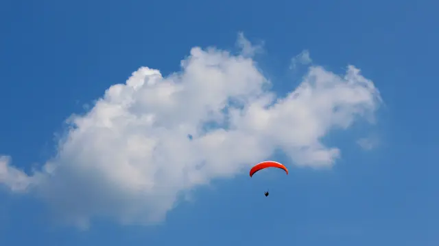 Parapentiste en vol sous un ciel bleu avec nuages blancs, voile de parapente orange visible en pleine altitude vers Aubagne