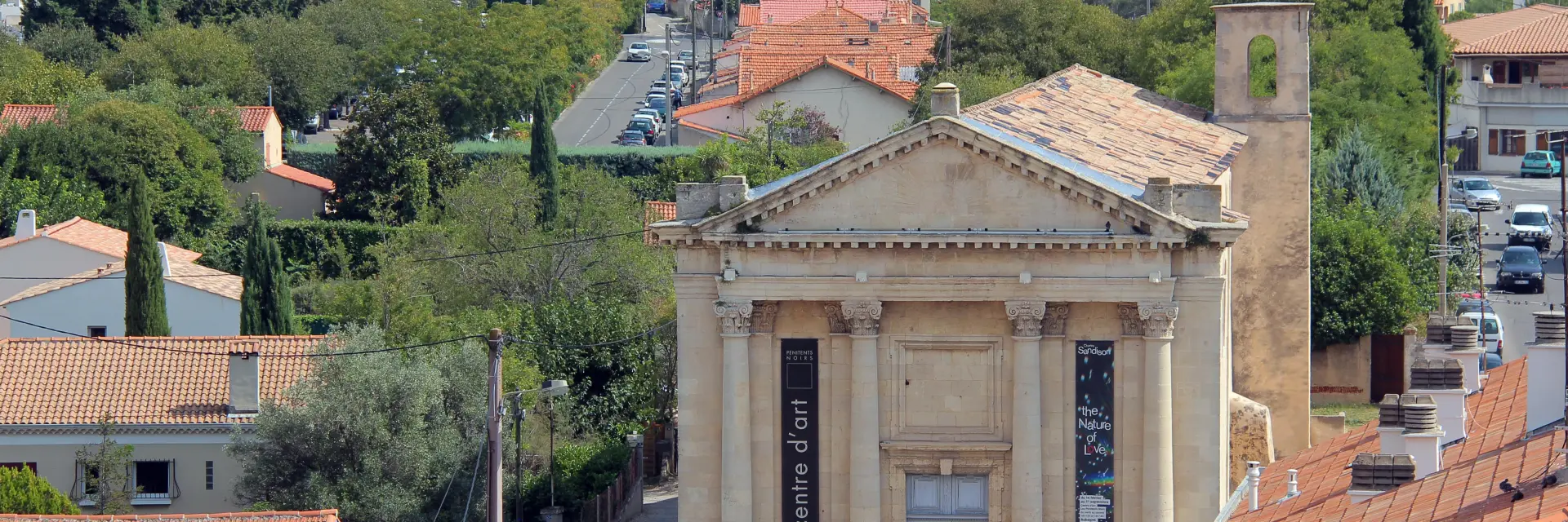 Façade du centre d’art des Pénitents Noirs à Aubagne, entouré de toits provençaux et de collines.