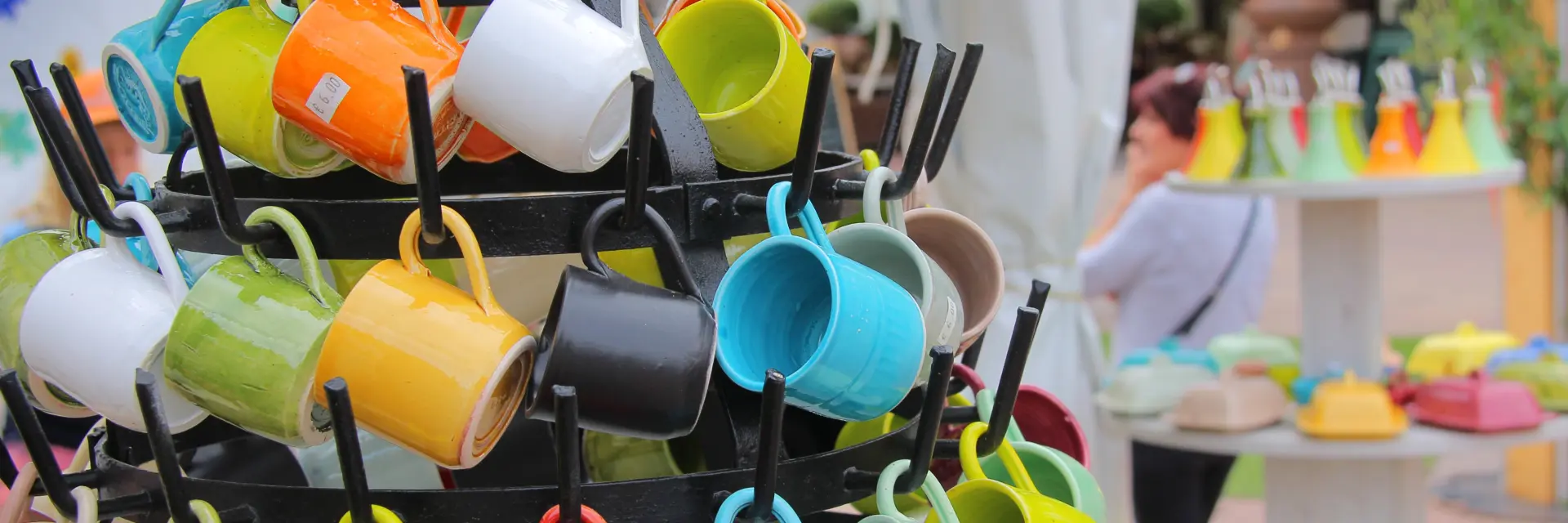 Tasses en céramique multicolores accrochées sur un présentoir lors d’un marché artisanal en plein air.