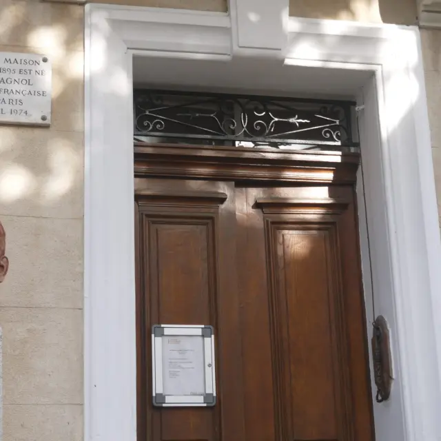 Façade de la maison natale de Marcel Pagnol à Aubagne avec porte en bois, plaques commémoratives et buste de l’écrivain.