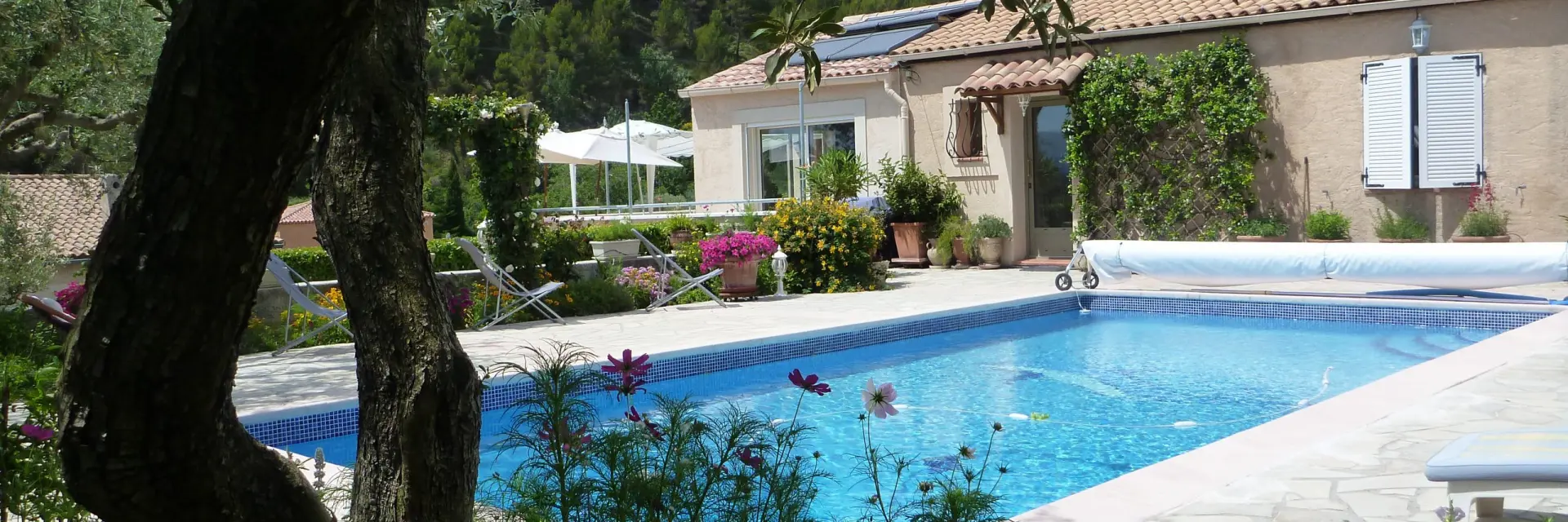 Piscine extérieure avec eau bleue, terrasse claire, maison de plain-pied et jardin fleuri entouré d’arbres et de végétation à la Chambre d'hôtes le 13 original à Saint-Savournin