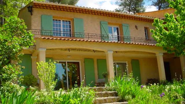 Maison provençale à deux niveaux avec façade claire, volets verts, terrasse couverte et jardin arboré au premier plan. Location de vacances à Auriol, Pays d'Aubagne et de l'Etoile
