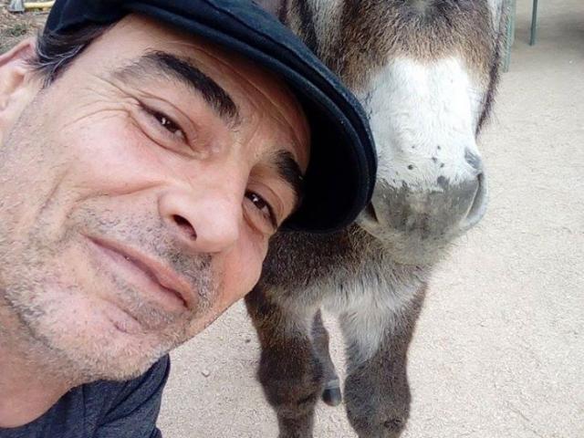 Homme souriant posant aux côtés d’un âne dans un environnement naturel au domaine de Font de Mai à Aubagne