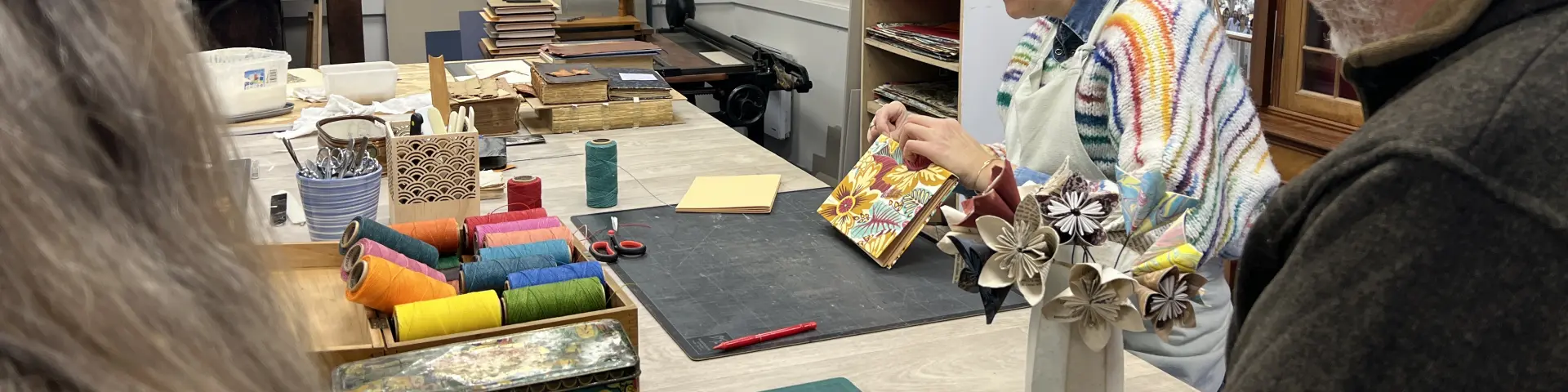 Personnes observant une relieuse artisanale travaillant sur la couverture d’un livre dans un atelier de reliure.
