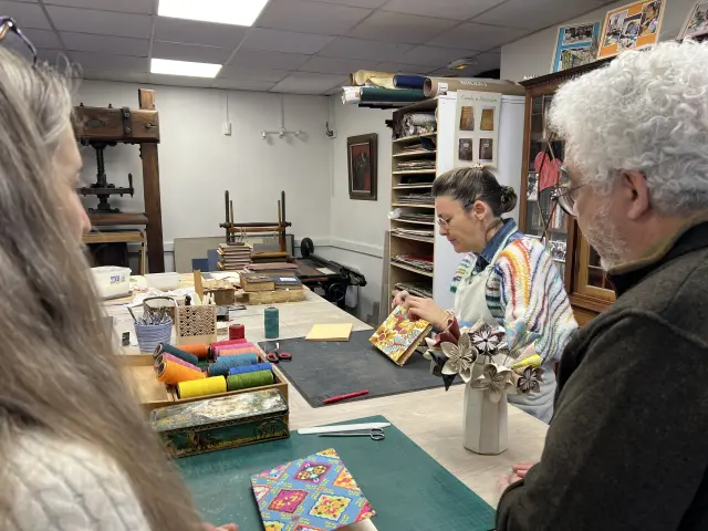 Personnes observant une relieuse artisanale travaillant sur la couverture d’un livre dans un atelier de reliure.