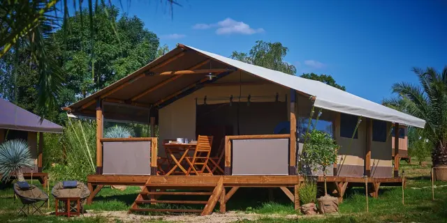 Hébergement de plein air type lodge en bois avec terrasse couverte, mobilier extérieur et vue sur un environnement naturel verdoyant au camping du Garlaban à Aubagne
