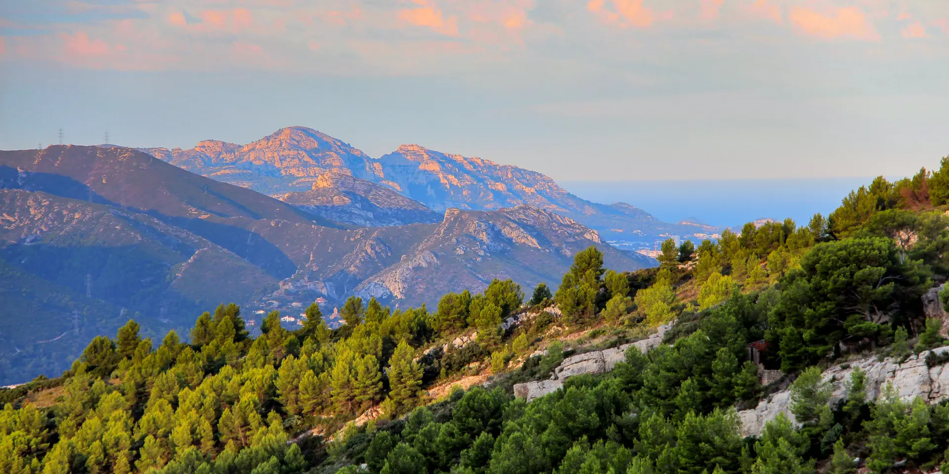 Paysage panoramique du massif de l’Étoile en Provence avec collines boisées de pins, reliefs rocheux et ciel pastel au lever du soleil.