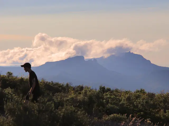 Randonneur marchant dans la garrigue du massif du Garlaban avec vue sur les reliefs montagneux et les nuages en Provence.