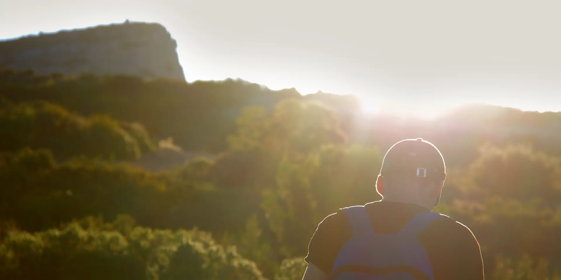 Un randonneur équipé d’un sac à dos marche sur un sentier de garrigue au lever du soleil, face au paysage naturel méditerranéen d'Aubagne