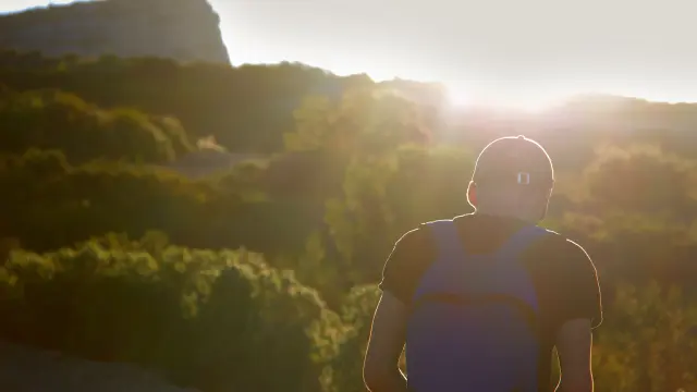 Un randonneur équipé d’un sac à dos marche sur un sentier de garrigue au lever du soleil, face au paysage naturel méditerranéen d'Aubagne
