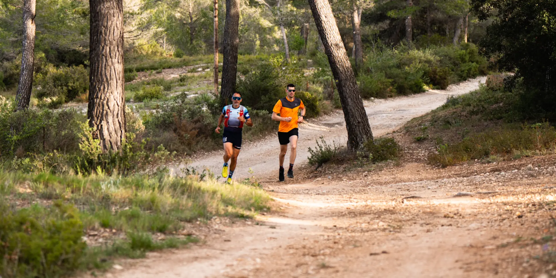 Deux coureurs de trail arpentent un sentier en terre au cœur d’une forêt de pins provençale, en pleine nature dans le Pays d'Aubagne et de l'Étoile