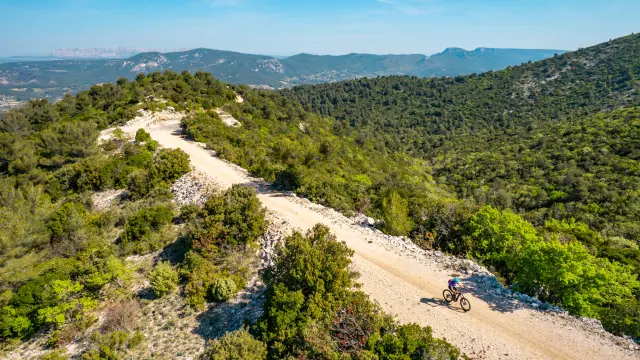Cycliste sur une piste de terre traversant un massif naturel couvert de végétation méditerranéenne, avec collines et forêts en arrière-plan à Aubagne