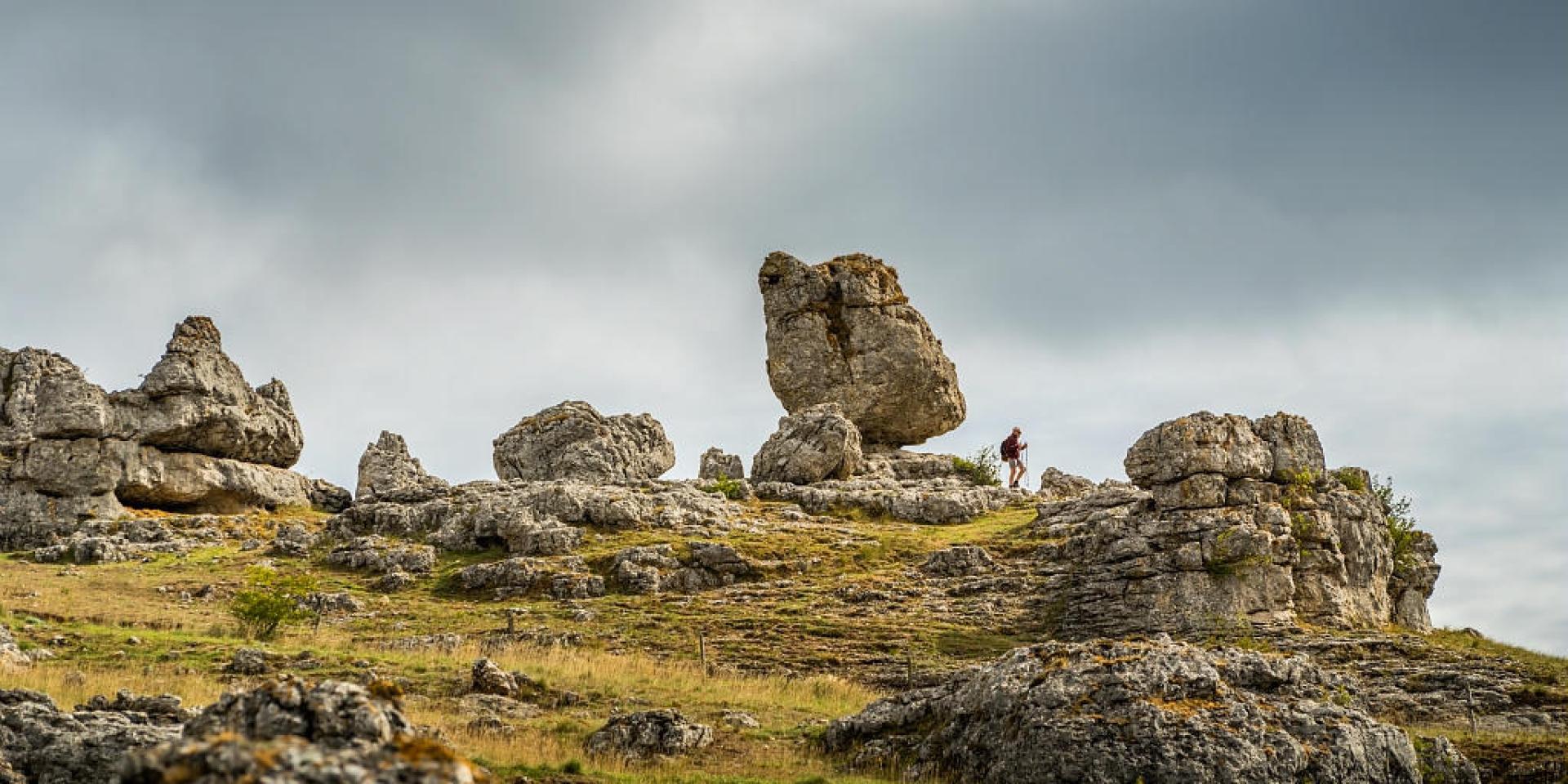 A hiker strolls through a group of large rocks of various shapes forming the chaos of Nîmes-le-Vieux on the Causse Méjean.