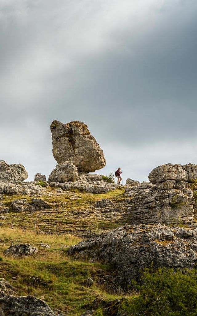 A hiker strolls through a group of large rocks of various shapes forming the chaos of Nîmes-le-Vieux on the Causse Méjean.