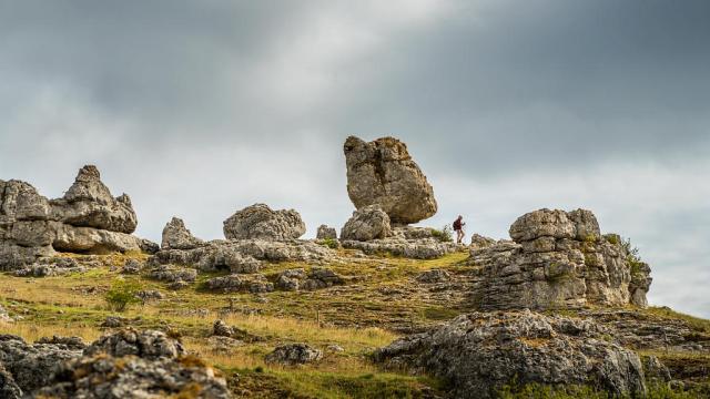 Un randonneur se balade à travers un ensemble de grandes roches aux formes variées formant le chaos de Nîmes-le-Vieux sur le Causse Méjean