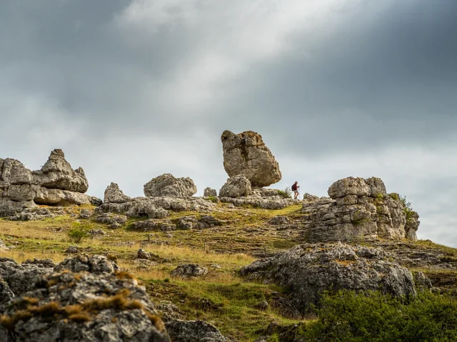 A hiker strolls through a group of large rocks of various shapes forming the chaos of Nîmes-le-Vieux on the Causse Méjean.