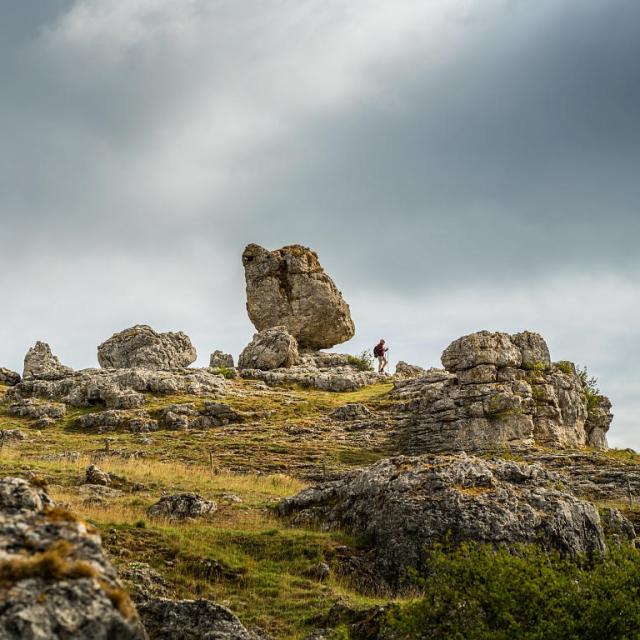 A hiker strolls through a group of large rocks of various shapes forming the chaos of Nîmes-le-Vieux on the Causse Méjean.