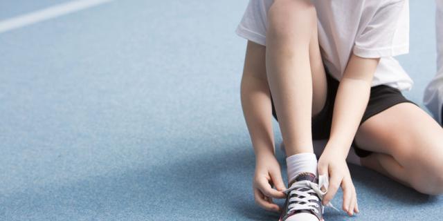 Cropped photo of a young boy tying his sports shoes on the court