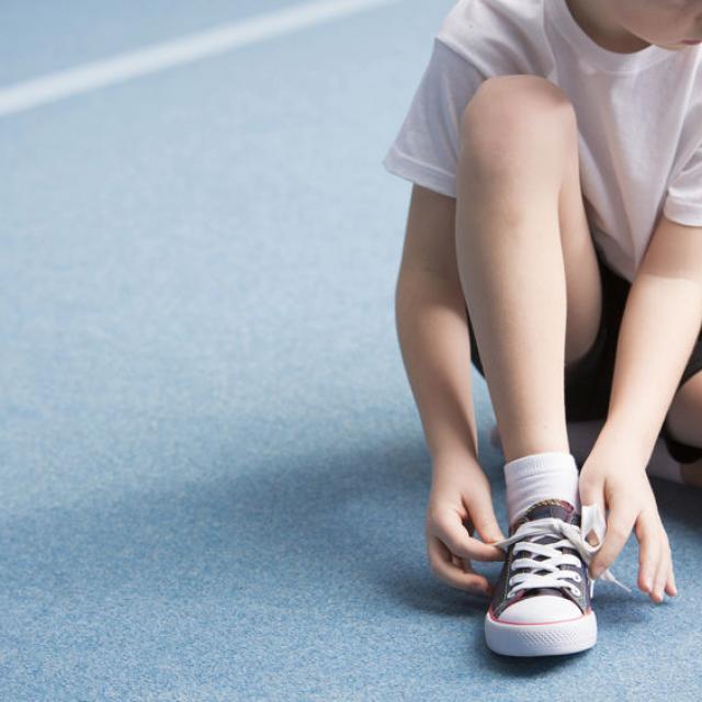 Cropped photo of a young boy tying his sports shoes on the court