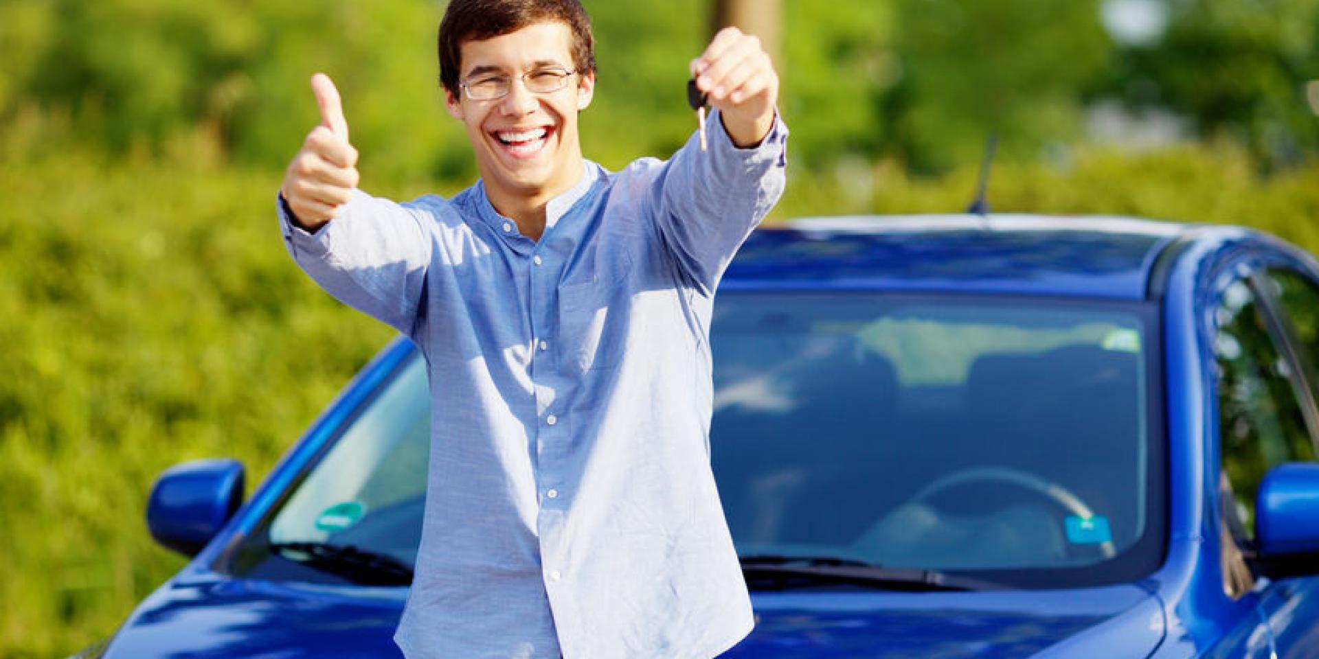 Young happy man in glasses standing in front of his new car and showing thumb up and car key