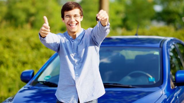 Young happy man in glasses standing in front of his new car and showing thumb up and car key